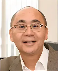 A man with glasses and a suit is smiling.